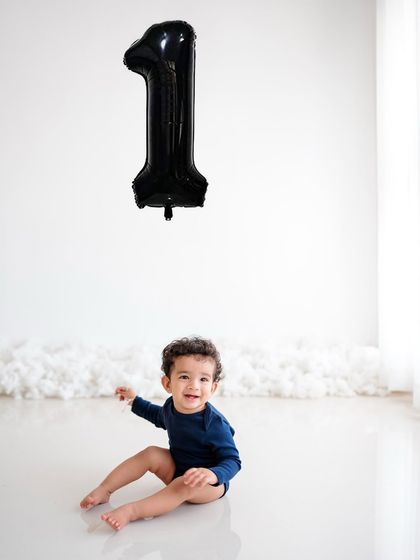 A minimalist first birthday shoot with a simple "1" balloon. The focus is all on the birthday boy's happy smile.