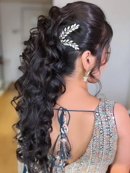 A chic and voluminous ponytail for a Sangeet night. The soft curls and elegant hair accessory create a look that is both modern and perfect for dancing the night away.