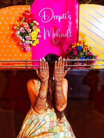 The bride hides her face behind her hands, creating a striking image that puts her full-arm mehandi in the spotlight.