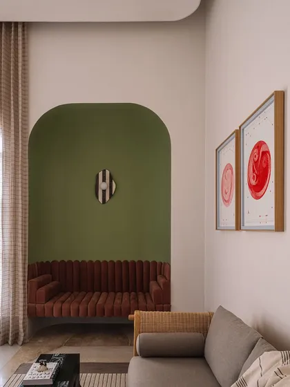 The home office at Rehethaan is bathed in morning sunlight. The space features a comfortable seating area with a sofa nestled in an olive-green archway, creating a perfect spot for breaks between work.