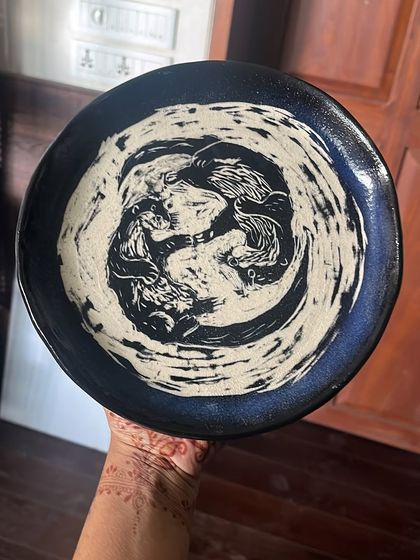 A close-up of a finished Sgraffito plate featuring a dynamic, swirling design. The contrast between the dark glaze and the light clay underneath creates a powerful visual effect.