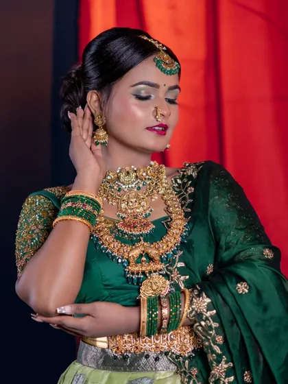 A close-up of a half-saree look. The model wears layers of temple jewellery, and the makeup features a bold lip and shimmery eyes.