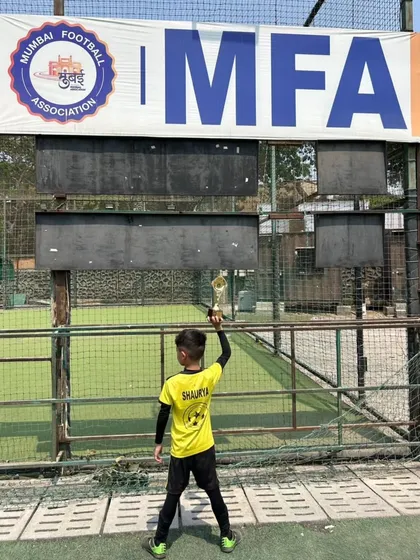 Shaurya Parikh, our Man of the Match, holding his trophy high in front of the MFA scoreboard. A proud moment for a dedicated player.