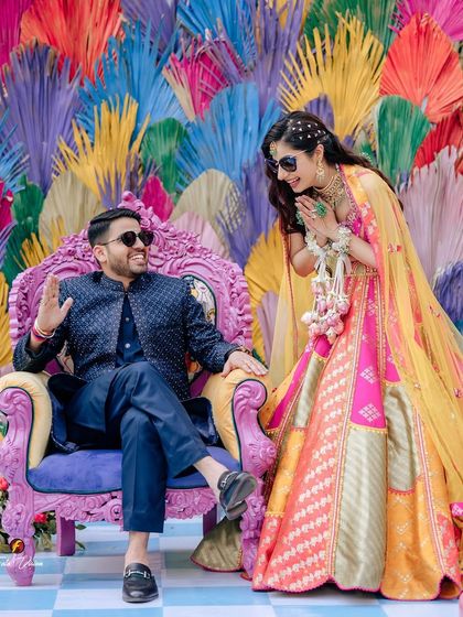 A playful, royal-themed moment from a Mehendi, with the bride greeting her groom who is seated on a throne-like chair.