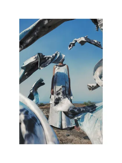 A surreal and artistic image from the Adiv campaign. The styling involves wrapping the model and the landscape in fabric, blurring the lines between the human form and the natural environment.