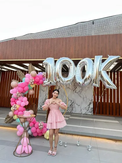 The final look of the 100k celebration decor, with the influencer happily posing in front of the backdrop. We love bringing our clients' visions to life for their most important milestones.