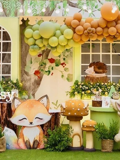 A whimsical corner of Ryne's woodland party, featuring a sleepy fox, a rabbit, and a hedgehog prop. The window-pane backdrop and green balloon garland add to the enchanted forest feel.