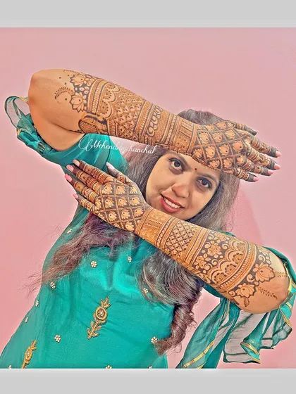 A happy bride posing with her full bridal mehendi. The design is intricate, and the stain is beautifully dark.