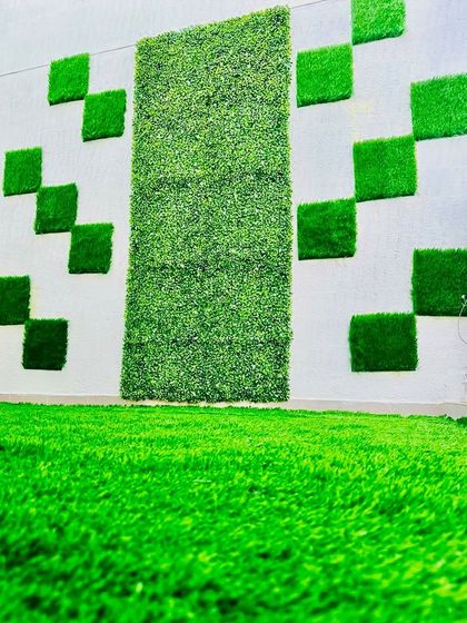 A creative and modern exterior wall design. We used square artificial grass tiles arranged in a scattered, pixel-like pattern to create a playful and artistic effect on this white wall.