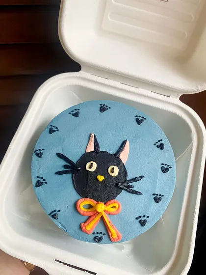 This bento cake features a portrait of a black cat with a bright bow, surrounded by tiny paw prints. It's a perfect little treat for any cat lover.