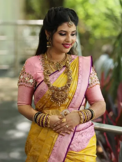 A full view of a beautiful bridal look. The custom-designed pink blouse with three-dimensional floral embroidery pairs wonderfully with the traditional yellow Kanjivaram silk saree.