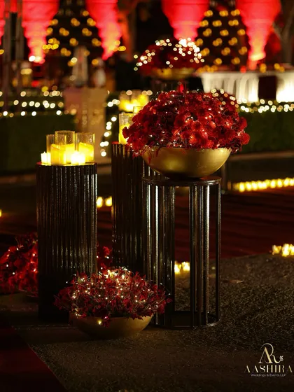 A beautiful arrangement of red roses in golden bowls, placed on tiered lattice stands and surrounded by the soft light of candles.