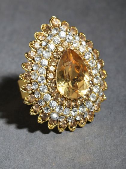 A beautiful adjustable ring with a large yellow stone in a teardrop shape, surrounded by sparkling stones.