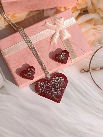 This heart-shaped jewelry set, with a large pendant and matching stud earrings, is made with a deep red color and sparkling glitter. It's a perfect gift for someone you love.