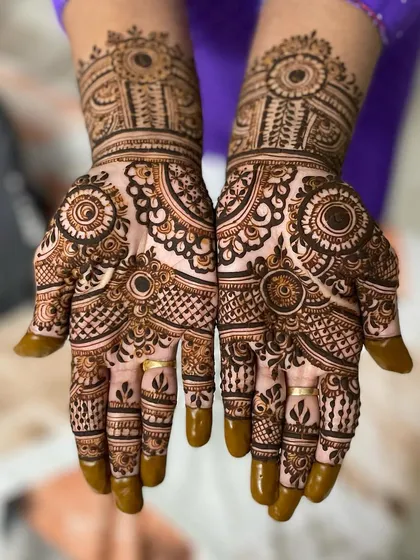 This symmetrical design features bold circular motifs and intricate line work. The solid henna on the fingertips provides a classic contrast to the detailed patterns on the palms.