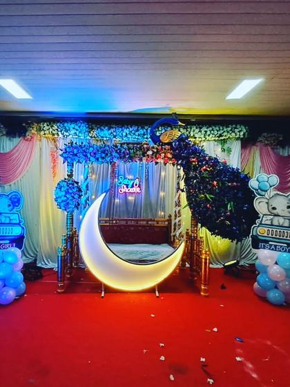 A beautiful baby shower stage with a peacock made of blue flowers on a traditional swing. The lighted moon and elephant-themed cutouts add to the charm.