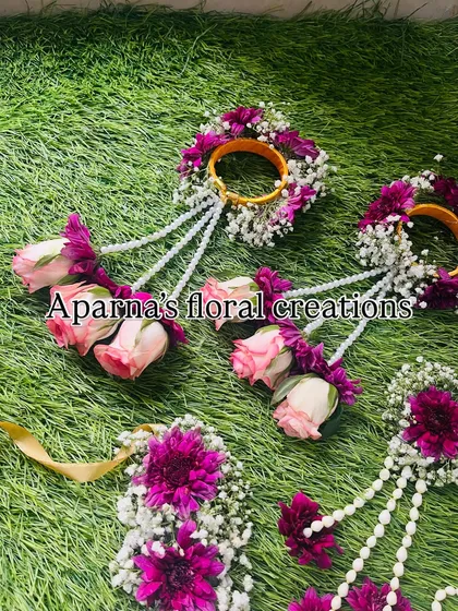 A Haldi jewellery set for a bride and her bridesmaids. This set features haath phool and kaliree made with pink roses, purple chrysanthemums, and baby's breath.
