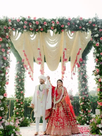 The couple stands under a beautiful floral mandap, celebrating their union with a shower of petals.