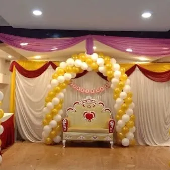 A classic stage decoration for a baby shower or naming ceremony, with a yellow and white balloon arch and a special chair.