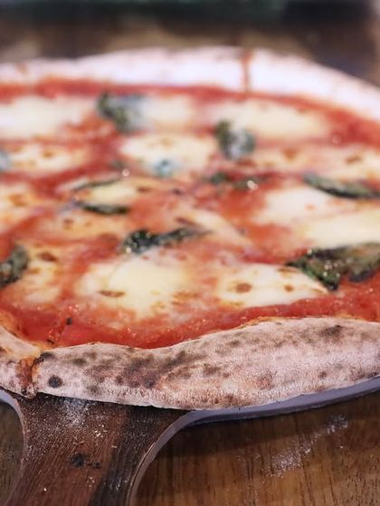 A classic Margherita on a wooden peel, just as it comes out of the oven. The cheese is perfectly melted, and the basil is fragrant from the heat.