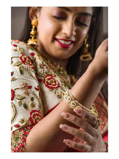 A close-up shot focusing on the detailed floral embroidery of the blouse and the delicate design of the gold bangle. This highlights the craftsmanship of both the apparel and accessories.