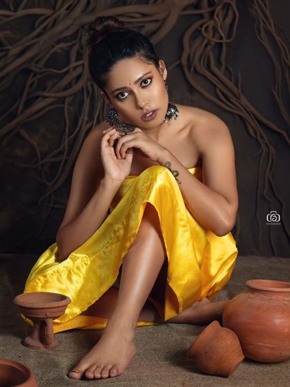 A close-up from the yellow satin series, focusing on the model's expression and the traditional silver earrings. The background of dark, tangled roots adds a raw, natural element to the studio setup.