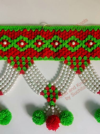 A close-up of the classic red and green Moti toran, showing the detailed crochet work and pearl embellishments.