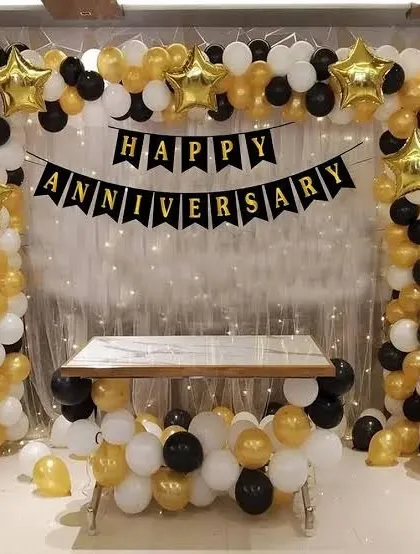A classic anniversary decoration with a black, gold, and white balloon arch and a 'Happy Anniversary' banner.