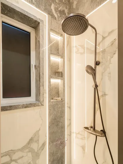 This bathroom features a beautiful combination of fluted textures and ambient LED grooves. The rain shower head and recessed niches in the shower area create a spa-like experience.