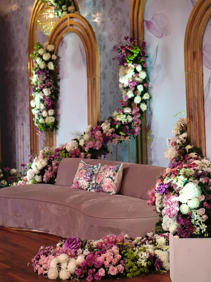 A close-up of a plush, curved sofa surrounded by a sea of purple and white flowers. The floral-print cushion adds a perfect finishing touch to this romantic photo-op.