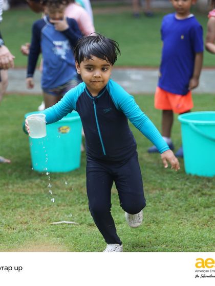 A young student runs with a cup of water during the Pre-K wrap-up party. These moments of pure fun are essential for building positive early learning experiences and friendships.