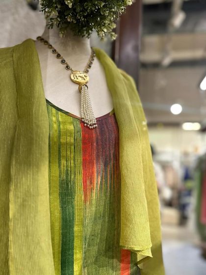 A detailed shot of the multi-colored striped tunic, layered under a chartreuse shrug and accessorized with a beautiful pendant necklace.