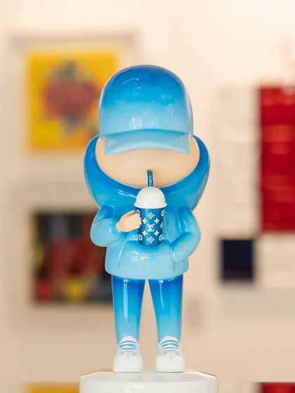 Another piece from the "Kid Cup" series, this one in a cool aqua blue. The figure holds a cup adorned with luxury monograms, blending youth culture with high fashion.