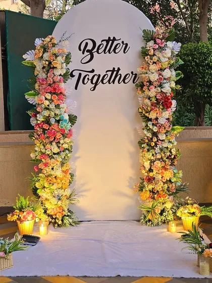 A beautiful and lush floral backdrop for a romantic celebration. I used two large pillars of fresh, multi-colored flowers to frame a simple white panel with the message "Better Together," creating a perfect photo spot for the couple.