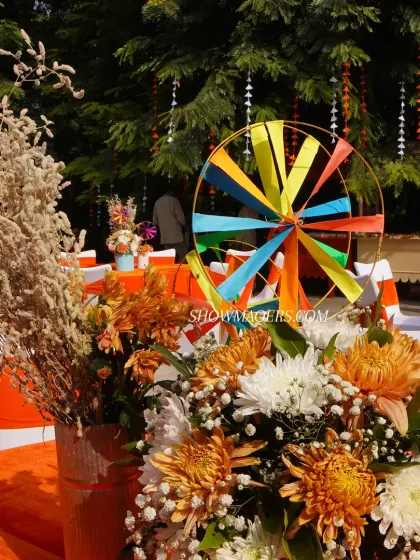 A close up of a table centerpiece featuring orange and white chrysanthemums and a colorful pinwheel, reflecting the playful theme.