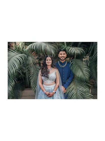 A lovely portrait of the engaged couple against a backdrop of lush palm leaves. Their coordinated blue outfits and happy smiles make for a stunning picture.