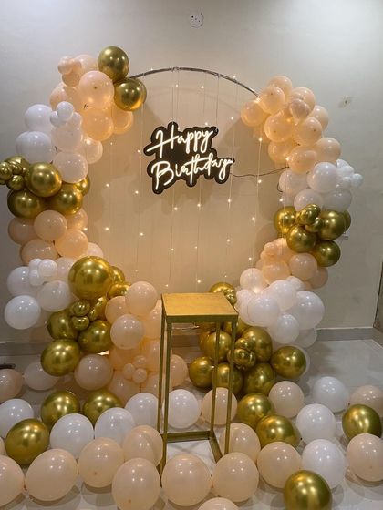 A peach, white, and gold balloon ring with a neon sign. The balloons scattered on the floor make the setup feel full and celebratory.