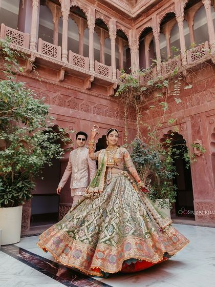The bride twirls in her ornate lehenga within the stunning red sandstone courtyard of the Bikaner palace, a perfect shot for a royal Rajasthani wedding.