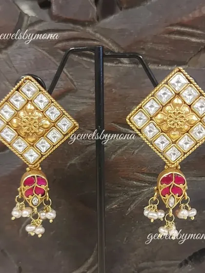 These Dakshinaya earrings showcase traditional South Indian design with a modern twist. The diamond-shaped stud features a floral motif and a ruby-colored drop, perfect for a classic, ethnic look.