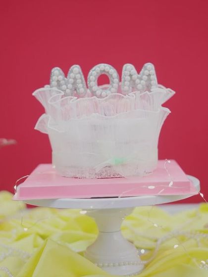 An elegant cake for "Mom," featuring a pearl-studded "MOM" topper and delicate lace-like details.