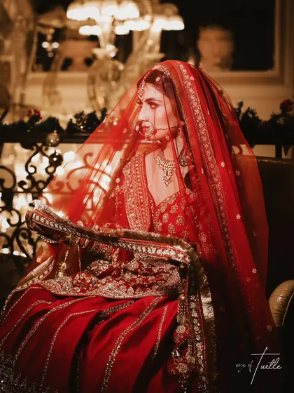 A moment of quiet reflection through the veil. The rich red tones and soft lighting create a classic, romantic bridal portrait that feels both intimate and timeless.