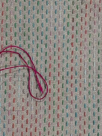 A piece of fabric showing the beginning of a Kasuti pattern. The loose pink thread is ready for the next stitch, illustrating the very start of the creative process.