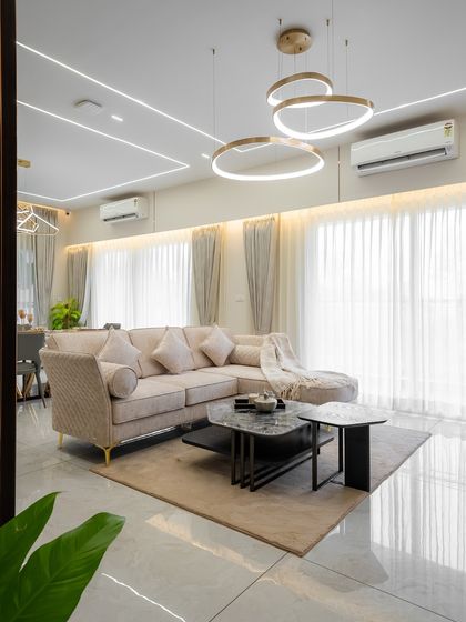 A bright and airy living space featuring a comfortable sectional sofa and modern ring chandeliers. The design uses a neutral palette and clean lines to create a feeling of layered luxury that soothes rather than shouts.