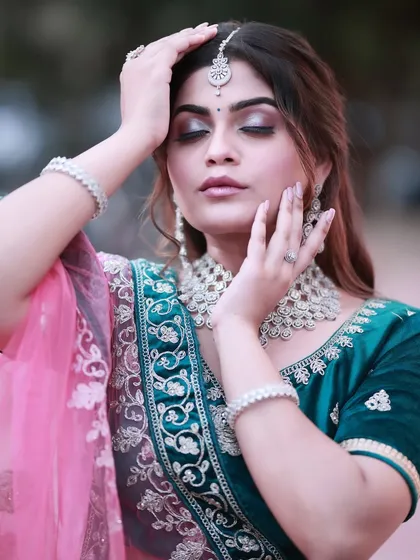 A modern and glamorous lehenga look. The bride is wearing a beautiful teal velvet lehenga, and the makeup is soft and shimmery, perfect for a reception or sangeet.