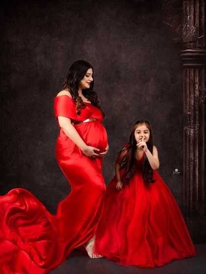 A beautiful family portrait with mother and daughter in matching red gowns. Including older siblings is a wonderful way to celebrate the growing family and create lasting memories.