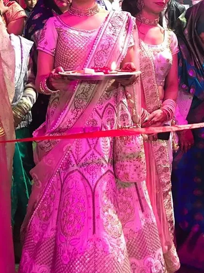 Our client participating in a wedding ritual while wearing the rented ivory lehenga. The outfit looks stunning even under the vibrant pink lighting of the event.