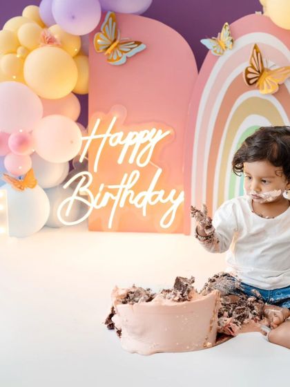 The birthday girl pauses her cake smash to look towards the camera, a funny and cute moment.