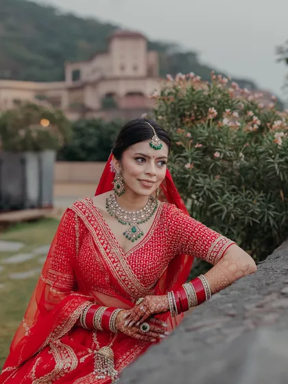 The bride, in her striking red lehenga, poses against the historic backdrop of Neemrana Fort-Palace, her elegance a beautiful contrast to the ancient stone.
