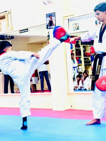 A student demonstrates a powerful side kick on a target held by a senior, showcasing the skills learned for his belt exam.