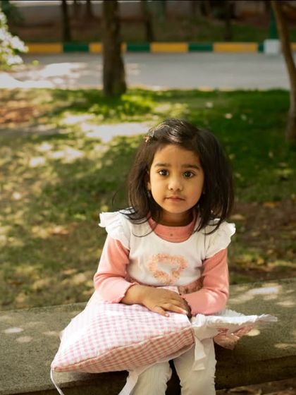 A sweet and simple outdoor portrait of a young girl sitting on a park bench. The natural light and her direct gaze create a beautiful, classic image.